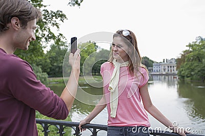 Young man photographing woman through cell phone at lakeside Stock Photo