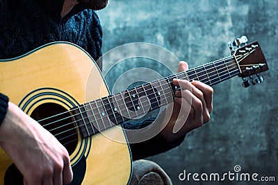 Young man playing an acoustic guitar on the background of a concrete wall Stock Photo