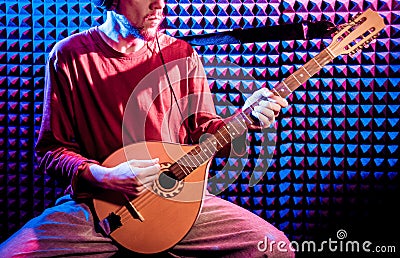 Young man playing on the bouzouki in sound recording studio. Stock Photo