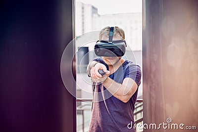 Young man playing shooting games in virtual reality headset on the urban building background outdoors. Technology, innovation, cyb Stock Photo