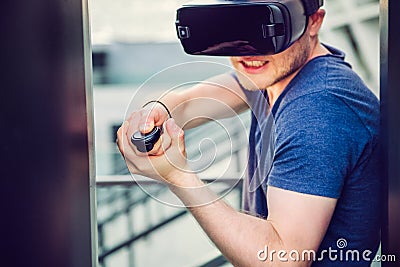 Young man playing shooting games in virtual reality headset on the urban building background outdoors. Technology, innovation, cyb Stock Photo