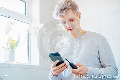 Young man puts the settings of his electronic toothbrush with mobile phone app. Wireless connecting sonic toothbrush Stock Photo