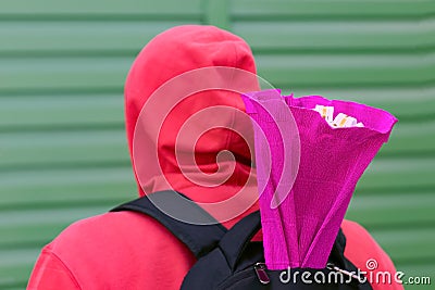 A young man in a red jacket with a hood on his head and a backpack on his back carries a gift in a bright package to his Stock Photo