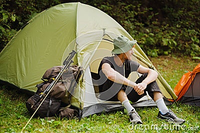 Young man resting in tent while hiking in green forest Stock Photo