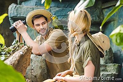 young man in safari suit with parrot on shoulder flirting with woman while hiking Stock Photo