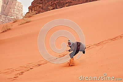 Young man sand dune surfing wearing bisht - traditional Bedouin coat. Sandsurfing is one of the attractions in Wadi Rum desert Stock Photo