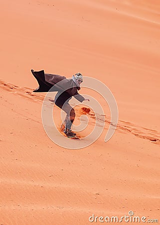 Young man sand dune surfing wearing bisht - traditional Bedouin coat. Sandsurfing is one of the attractions in Wadi Rum desert Stock Photo