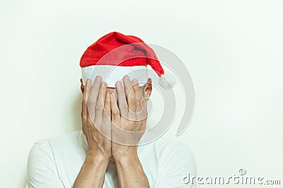 Young man with Santa Claus hat cover his face with his hands feeling lonely and sad for New Year and Christmas holiday depression Stock Photo