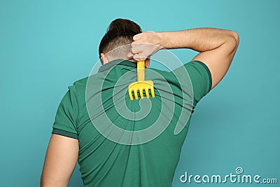 Young man scratching back with toy rake on color background. Stock Photo