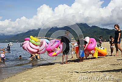 Young man sells and peddles ring lifebuoy on white sand beach Editorial Stock Photo