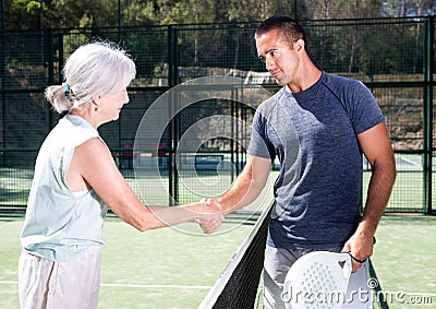 Young man and senior woman handshaking after padel tennis match Stock Photo