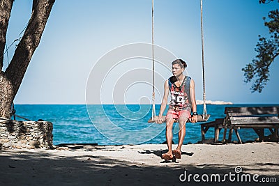 Young man sits on a rope swing on the beach on Ko Samet Stock Photo