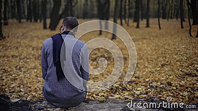 Young man sitting alone in autumn park, feels depression, nostalgia, loneliness Stock Photo