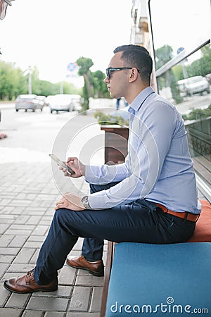 Young man is sitting on a bench with a smartphone in his hands. Stock Photo