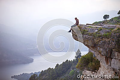 Young man sitting on edge of cliff and looking at river Stock Photo