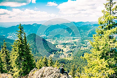 An young man sitting at the end of a rock, looking at the magnificent mountain aria view Stock Photo