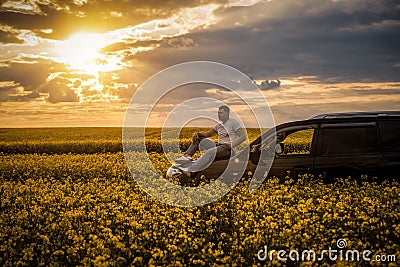 Young man sitting on the hood of a car at sunset Stock Photo