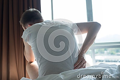 Young man sitting indoor on the bed feeling ache in his back Stock Photo