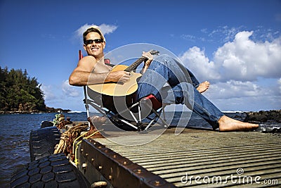 Young Man Sitting Lakeside and Playing Guitar Stock Photo