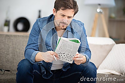 Young man sitting on sofa and doing crossword puzzle Stock Photo