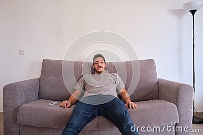 Young man sitting on a sofa watching television absorbed with his mouth opened Stock Photo