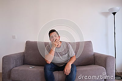 Young man sitting on a sofa yawning. Fatigue and tiredness concepts Stock Photo