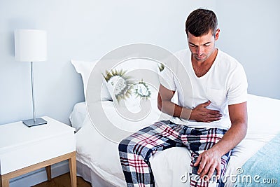 Young man sitting with stomach pain on bed Stock Photo