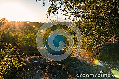 Young man sitting on stone and looking to Czech ore mountain valley at sunset landscape Stock Photo