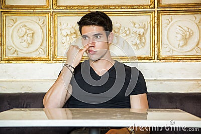 Young Man Sitting at Table Picking Nose Stock Photo