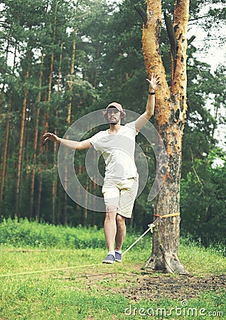 young man is slacklining walking and balancing on a rope, slackline outdoors Stock Photo