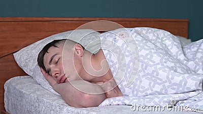A young man is sleeping with a funny expression on his face. A man lies in bed in his room. Stock Photo