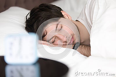 Young man sleeping next to alarm clock wearing smart wristband Stock Photo