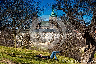 Young man sleeping under the trees of the Petrin Park with the Prague Cathedral on background Editorial Stock Photo