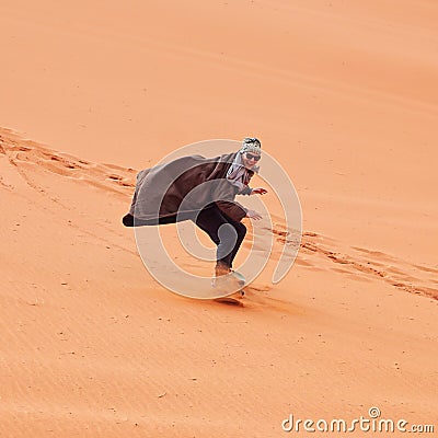 Young man smiling, sand dune surfing wearing bisht - traditional Bedouin coat. Sandsurfing is one of the attractions in Wadi Rum Stock Photo