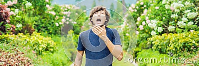 Young man sneeze in the park against the background of a flowering tree. Allergy to pollen concept BANNER long format Stock Photo