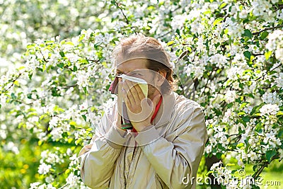 The young man sneezes on a background of a blossoming Apple tree Stock Photo