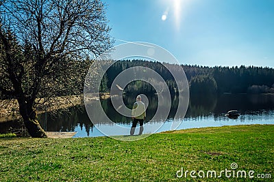 Young man stand on nice clean pond with wooden building and spring tree with blue sky Stock Photo