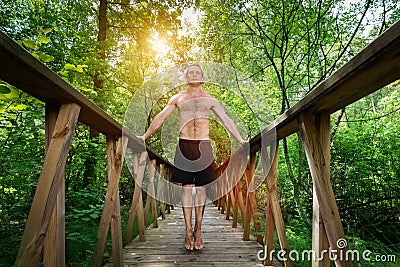 Young man standing on a footbridge in the forest. Stock Photo