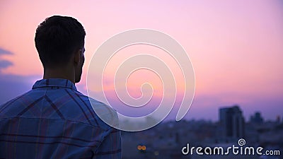 Young man standing on roof of building alone and meditating, enjoying freedom Stock Photo