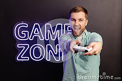 Young man standing at the wall in the room and playing, holding wireless joystick, screaming, and winning intense video game match Stock Photo