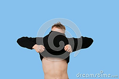 Young man struggling to pull down t-shirt over blue background Stock Photo
