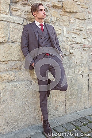 Young man with a suit and tie is waiting for a person near a stone wall Stock Photo