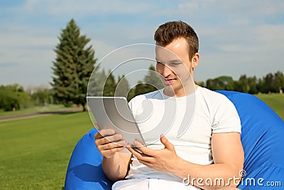 Young man with tablet PC resting on bean bag chair outdoors Stock Photo