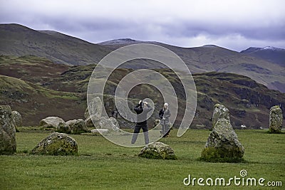 Young man taking photo of young woman and dogs on cellphone at Castlerigg Stone Circle in English Lake District Editorial Stock Photo