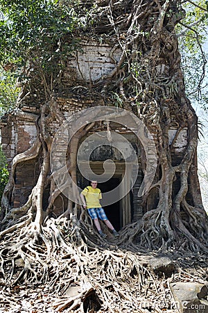 young man, the teenager at an entrance to the destroyed covered with roots of trees temple Prasat Chrap in the Koh Ker temple com Stock Photo