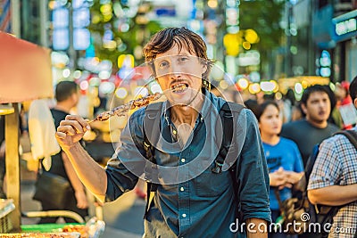 Young man tourist eating Typical Korean street food on a walking street of Seoul. Spicy fast food simply found at local Editorial Stock Photo