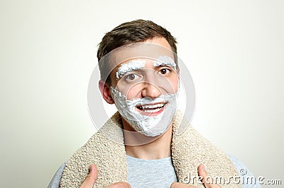 Young man with towel on shoulders and foam beard and eyebrows smiles into mirror Stock Photo