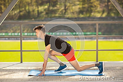 Young man training yoga outdoors. Sporty guy makes stretching exercise on a blue yoga mat, on the sports ground Stock Photo