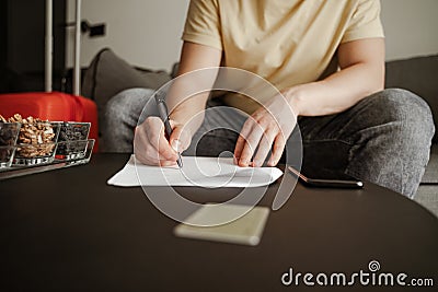 Young man traveler is sitting on couch and filling documents in hotel room on summer vacation. Cool male in casual Stock Photo