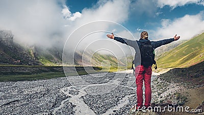 Young man traveler walking and enjoys view of summer spring mountains, rear view with copy-space. Concept of achieving motivation Stock Photo